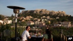 Tourists eat at a restaurant-cafe bar in front of the ancient Acropolis hill in central Athens, Greece, May 31, 2016.