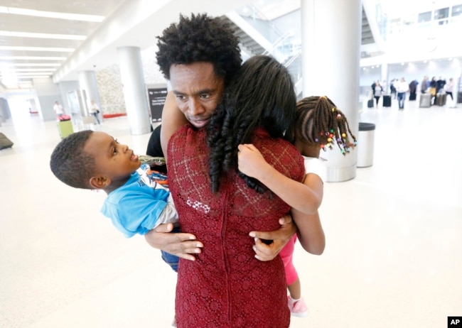FILE - Olympic silver medalist Feyisa Lilesa, rear, of Ethiopia, hugs his wife, Iftu Mulia, his daughter, Soko, right, 5, and son, Sora, left, 3, while picking up his family at Miami International Airport, Feb. 14, 2017.