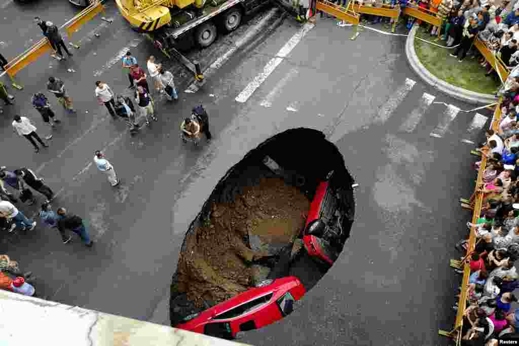 People gather near the scene where two vehicles have fallen into a sinkhole on a street in Harbin, Heilongjiang province, China, Aug. 4, 2018.