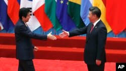 FILE - Japanese Prime Minister Shinzo Abe, left, and Chinese President Xi Jinping approach each other for a handshake before a group photo session for the G-20 Summit in Hangzhou, in eastern China's Zhejiang province, Sept. 4, 2016. The two will meet Thursday, when Abe starts a three-day visit to China.