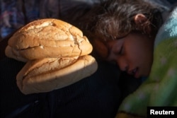 A girl, part of a caravan of thousands of migrants from Central America en route to the United States, sleeps next to bread donated by a passer-by in Tapachula, Mexico, Oct. 22, 2018.