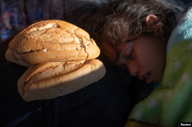 A girl, part of a caravan of thousands of migrants from Central America en route to the United States, sleeps next to bread donated by a passer-by in Tapachula, Mexico, Oct. 22, 2018.