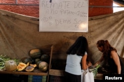 People shop at a vegetable street market in front of a whiteboard that reads "Auction of the year. Plantain 10.000 Bolivars per Kg. Everything else 5.000 Bolivars per Kg", in Caracas, Venezuela, Dec. 19, 2017.