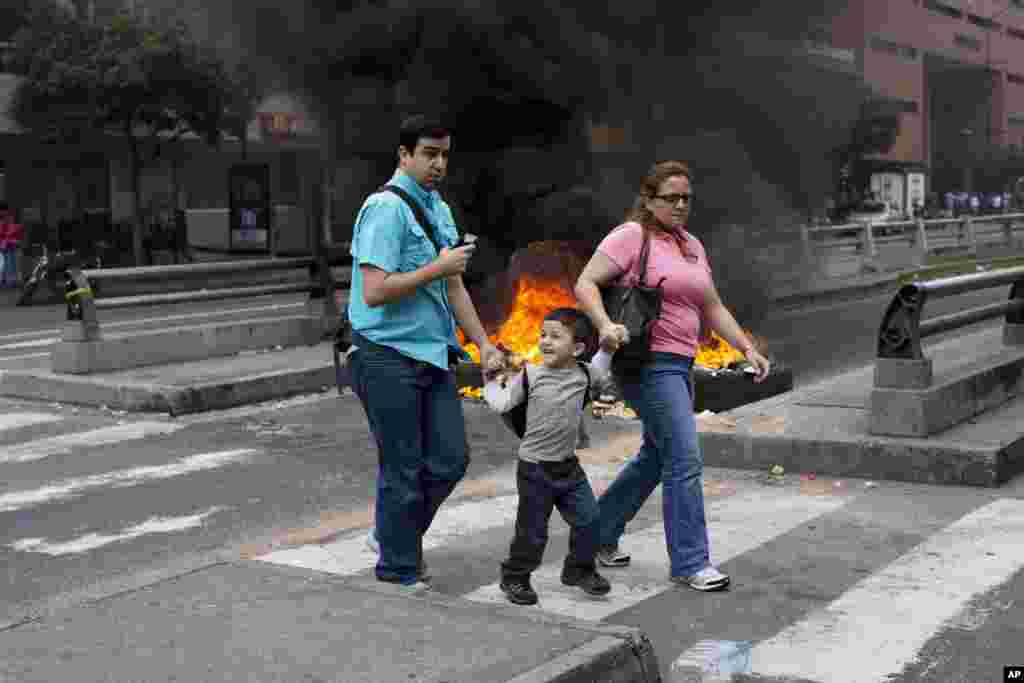 People walk in front of a burning barricade blocking the highway in Chacao, Caracas, Feb. 24, 2014. 