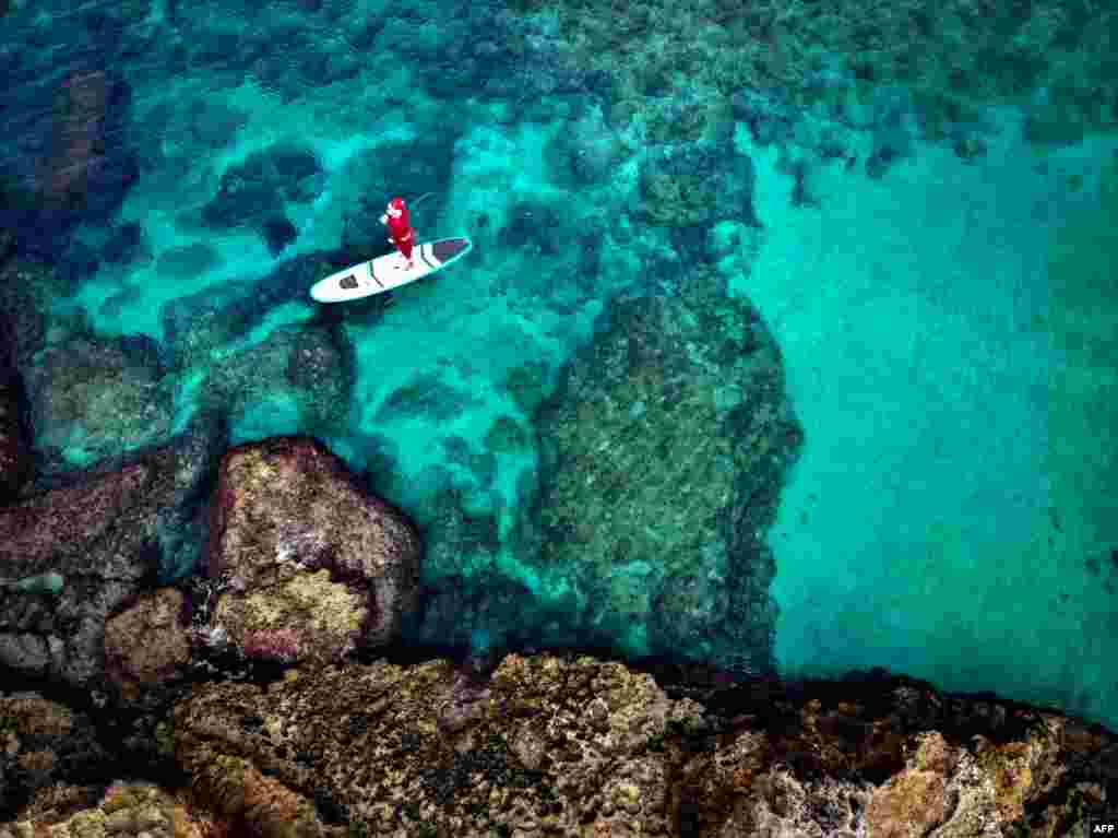 A man dressed with a Santa Claus outfit rides on a standup paddle in Lebanon&#39;s northern coastal city of Batroun.