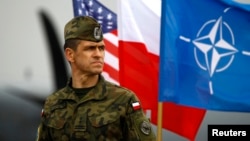 FILE - A Polish soldier stands in front of U.S., Polish and NATO flags ahead of military exercises in Swidwin, northwestern Poland, April 23, 2014.