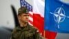 FILE - A Polish soldier stands in front of U.S., Polish and NATO flags ahead of military exercises in Swidwin, northwestern Poland, April 23, 2014.