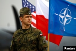 FILE - A Polish soldier stands in front of U.S., Polish and NATO flags ahead of military exercises in Swidwin, northwestern Poland, April 23, 2014.