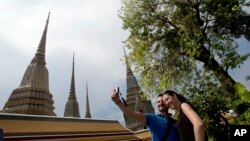 Western tourists snap a souvenir photo at a Wat Pho temple in Bangkok, Thailand.