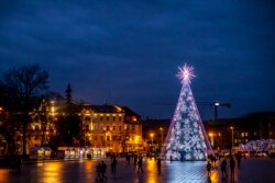 Orang-orang berjalan di dekat pohon Natal yang diterangi lampu di Cathedral Square di Vilnius, Lithuania, Selasa, 14 Desember 2021. (Foto: AP/Mindaugas Kulbis)