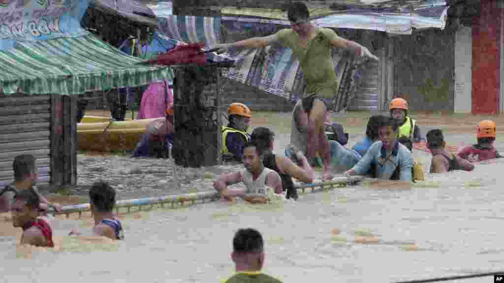 A resident balances himself as others cling to a railing after heavy monsoon rains spawned by tropical storm Fung-Wong flooded Marikina city, east of Manila, Philippines and most parts of the metropolis, Sept. 19, 2014.