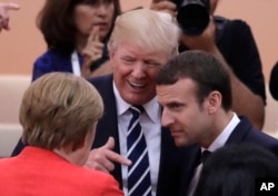 La canciller alemana Angela Merkel (de espaldas) conversa con el presidente de EE.UU. Donald Trump (centro) y con el presidente de Francia Emmanuel Macron, en el primer día de sesiones de la Cumbre del G20, en Hamburgo, Alemania. Julio 7 de 2017.