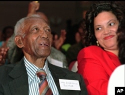 FILE - Tuskegee syphilis study survivor Ernest Hendon, 90, smiles while watching then-President Bill Clinton give a public apology, via video telecast, at the Kellogg Executive Conference Center in Tuskegee, Alabama, May 16, 1997. At right is Ethel Talley of the Macon County Health Department.