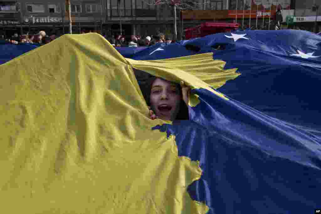 Seorang gadis Kosovo mengintip dari bendera nasional Kosovo raksasa yang dipajang pada perayaan HUT Kemerdekaan Kosovo ke-9 di Pristina.
