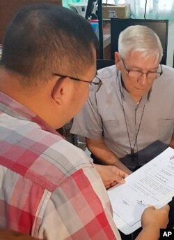 In this Bureau of Immigration photo, an American Roman Catholic priest, the Rev. Kenneth Bernard Hendricks, right, looks at documents after being arrested in a church in Naval in the island province of Biliran, central Philippines, Dec. 5, 2018.