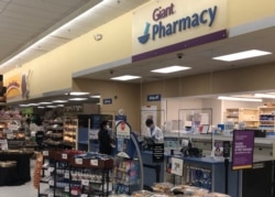 华盛顿近郊马里兰州一家药店工作人员戴上口罩并隔着临时挂起来的有机玻璃服务客户。(2020年4月1日)