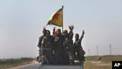 FILE - U.S.-backed Syrian Democratic Forces fighters stand on their pickup as the flash victory signs after battling the Islamic State militants, northeast Syria, July 26, 2017.