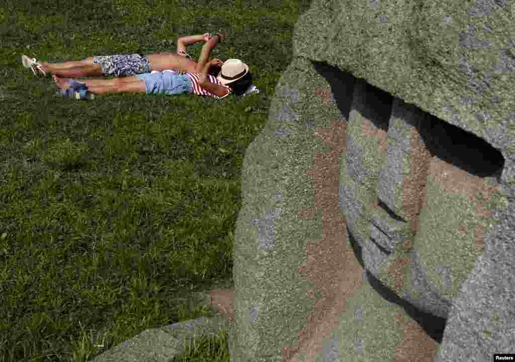 A couple suntans while lying on the grass, behind a statue, at the Odaiba Seaside Park in Tokyo, Japan. The temperature rose to 35 degrees Celsius (95 degrees Fahrenheit).