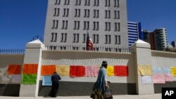 Una mujer pasa mientras un boliviano pega carteles de protesta en el muro de seguridad de la embajada de Estados Unidos durante una manifestación contra la intervención extranjera en Siria, en La Paz, Bolivia, el martes 3 de septiembre de 2013.