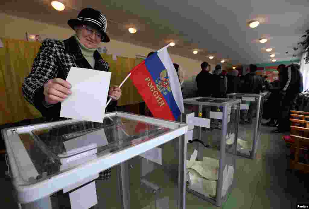 Uma mulher, com a bandeira da Rússia na mão, coloca o seu voto na urna, para o Refernedo sobre a região da Crimeia, numa mesa de voto em Bakhchisaray, Crimeia, Ucrânia, Março 16, 2014. 