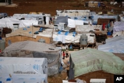 FILE - Syrian refugees stand outside their tents at a Syrian refugee camp in the town of Hosh Hareem, in the Bekaa valley, east Lebanon, Oct. 28, 2015.