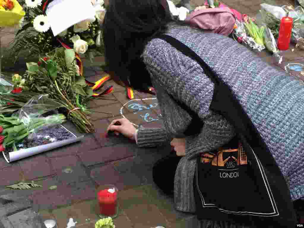 A woman draws a heart with her lipstick on the ground at a makeshift vigil near the Mealbeek metro station in Brussels, Belgium, March 24, 2016. (H. Murdock/VOA)