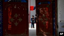 FILE - In this Sept. 20, 2018, file photo, an Uighur child plays alone in the courtyard of a home at the Unity New Village in Hotan, in western China's Xinjiang region. 
