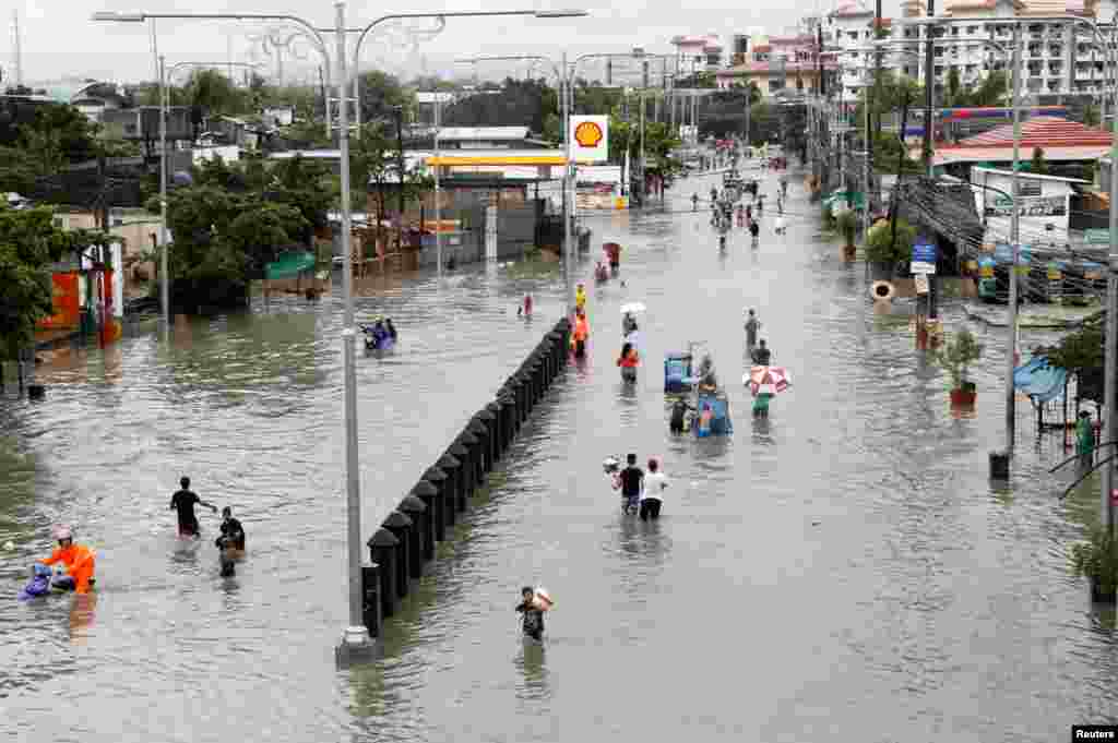 Residents wade and ride on pedicabs along a partially flooded road, in Las Pinas Metro Manila as a storm sweeps across the main Luzon island, Philippines.