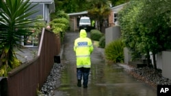 A police officer walks to a house to advise residents to evacuate as fears grow about possible storm surges at high tide in Ohope, New Zealand. 