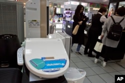 Shoppers stand near a smart toilet seat cover on display at a shopping mall in Beijing, China, April 20, 2016. The Chinese government's latest plan to perk up its slowing economy is based on the humble rice cooker and luxury toilet seats.