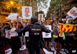 A Spanish national police officer tries to stop demonstrators protesting outside the main offices of the left wing party CUP in Barcelona, Spain, Sept. 20, 2017.