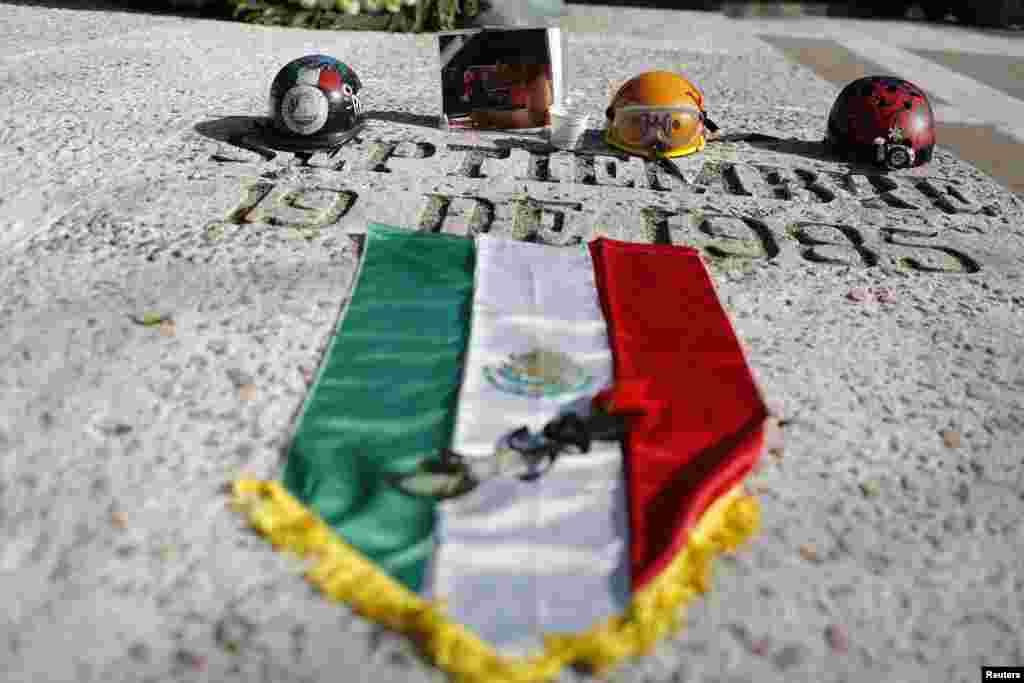 Helm dan foto seorang pekerja penyelamat yang tewas ditempatkan bersama bendera Meksiko pada saat peringatan ulang tahun ke-29 tragedi gempa tahun 1985, di Mexico City. Gempa pada tahun 1985 itu menewaskan sedikitnya 10.000 orang. &nbsp; 