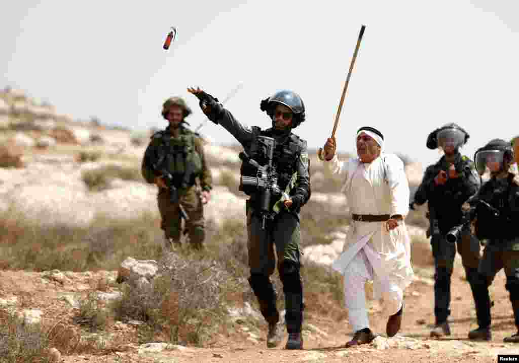 A Palestinian demonstrator gestures as an Israeli border police officer throws a sound grenade during a protest against Israeli settlement construction, in the village of Ras Karkar, near Ramallah in the occupied West Bank.