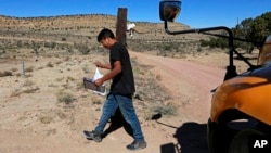 A student carries a math book delivered by school bus driver Kelly Maestas along his rural route outside Cuba, N.M., Oct. 19, 2020. (AP Photo/Cedar Attanasio)