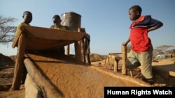 FILE - Two 13-year-old boys and one 15-year-old boy pour crushed gold ore over a sisal sack to concentrate the particles of gold at a processing site in Mbeya Reigon, Tanzania, in this 2013 photo.
