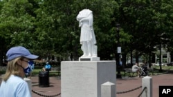 A passer-by walks near a damaged Christopher Columbus statue, Wednesday, June 10, 2020, in a waterfront park near the city's traditionally Italian North End neighborhood, in Boston.