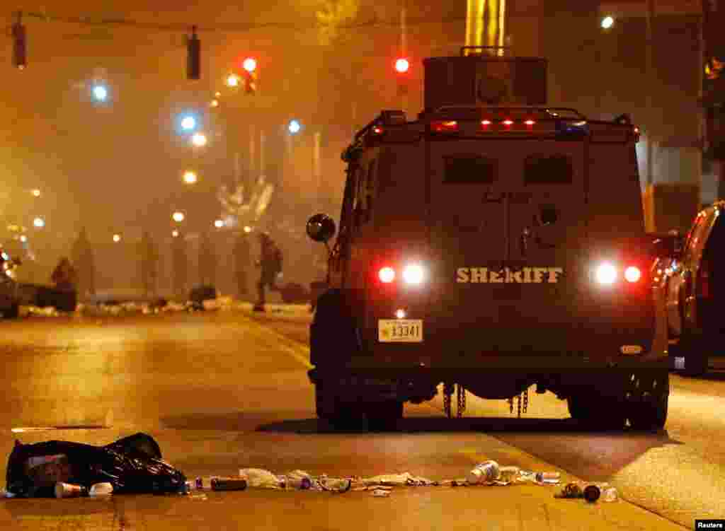 A police armored car moves down a street as clouds of smoke and crowd control agents rise shortly after the deadline for a city-wide curfew passed in Baltimore, April 28, 2015.