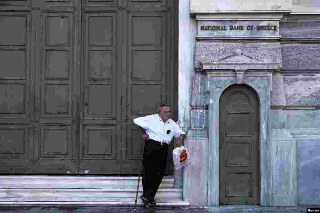 A pensioner waits outside a closed National Bank branch at the bank's headquarters in Athens, June 29, 2015. 