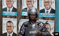 FILE - A Ugandan riot policeman blocks the gate of the party headquarters of opposition leader Kizza Besigye, shortly after raiding the premises for the second time in a week, in the capital Kampala, Uganda, Feb. 22, 2016.