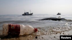 FILE - A plastic bottle and a tire are seen near a fishing boat on Fundao beach in Guanabara Bay in Rio de Janeiro, March 13, 2014. 