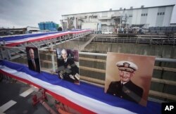 FILE - Near the portraits, from right, of John S. McCain, John S. McCain, Jr. and John S. McCain III, Navy Secretary Richard Spencer and his wife Polly Spencer disembark from the USS John S. McCain after a rededication ceremony at the U.S. Naval base in Yokosuka, southwest of Tokyo, July 12, 2018.