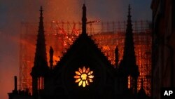 Flames and smoke rise from Notre Dame cathedral as it burns in Paris, Monday, April 15, 2019. Massive plumes of yellow brown smoke is filling the air above Notre Dame Cathedral and ash is falling on tourists and others around the island that marks the center of Paris. (AP Photo/T