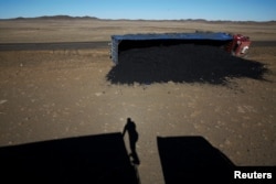 A photographer casts his shadow near a coal truck that flipped over at Khanbogd Soum, near the border with China in the Gobi desert, Mongolia, Oct. 29, 2017. Getting to the border can be a harrowing ordeal, as vehicles speed toward China and back down a one-lane road.