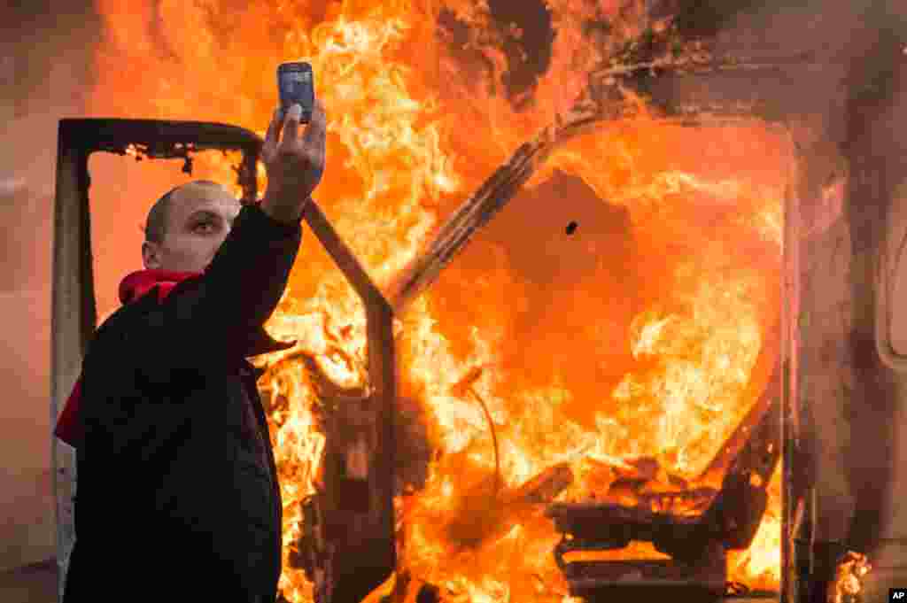 A protester takes a selfie in front of a burning car during a national trade union demonstration in Brussels, Belgium, Nov. 6, 2014. 