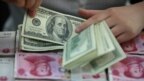 （资料图）中国的一位银行出纳员在一堆人民币百元大钞上清点美元。