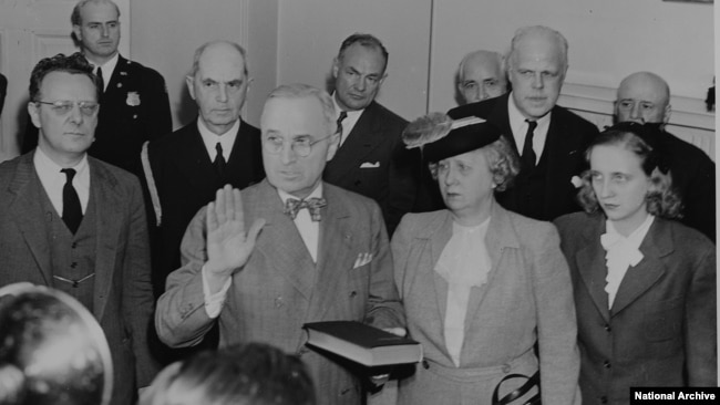 Bess and Margaret Truman stand beside Harry Truman as he takes the oath of office.