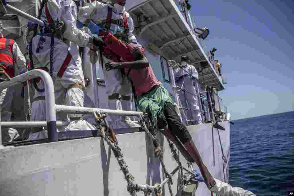 A migrant is pulled up onto a vessel by members of the Italian Coast Guard in the central Mediterranean Sea.