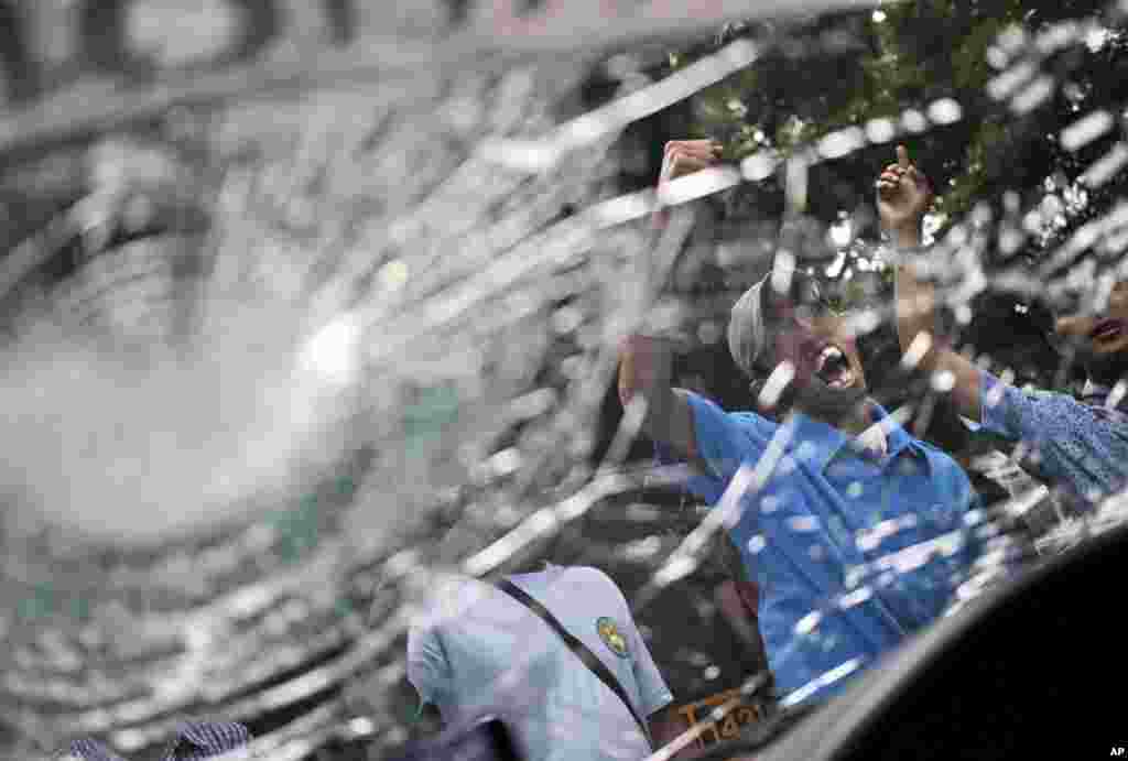 Taxi drivers are seen through the smashed windshield of a taxi as they shout slogans during a protest against ride-hailing apps such as Uber and Grab in Jakarta, Indonesia.