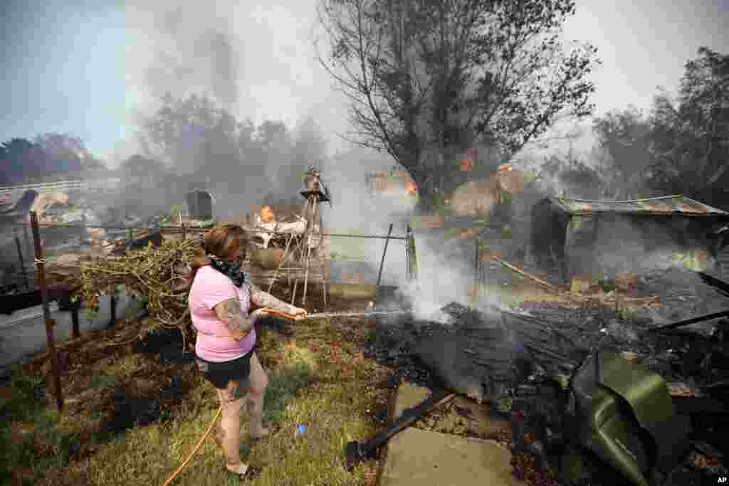 A woman douses water from a hose around her home as her neighbor's home burns during a wildfire in Escondido, California, May 15, 2014.