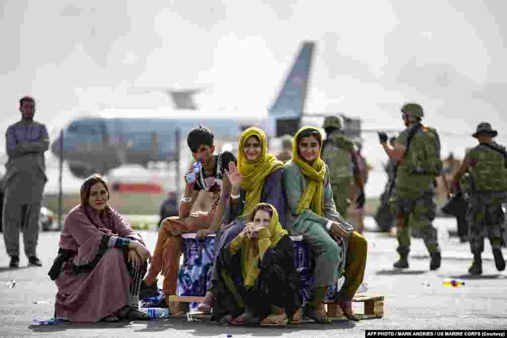 کابل کے حامد کرزئی انٹرنیشنل ایئرپورٹ پر ایک افغان خاندان بیرونِ ملک روانگی کا منتظر ہے۔ عقب میں امریکی بحریہ کا فضائی طیارہ نظر آ رہا ہے۔